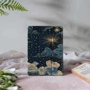 May include: A dark blue tablet case with a celestial design in gold. The design features clouds, stars, and a sunburst. The case is a folio style, designed to protect the tablet screen.