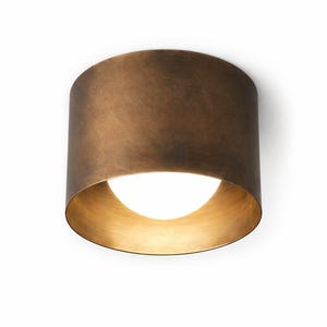 May include: A cylindrical, bronze-coloured ceiling light fitting with a warm, golden interior. The light fitting has a rounded, open bottom, revealing a bright, white light source. The fitting is mounted on a white surface.