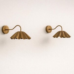 Pair of vintage brass wall sconces with downward, ruffled shades and curved arms, antique brass finish.