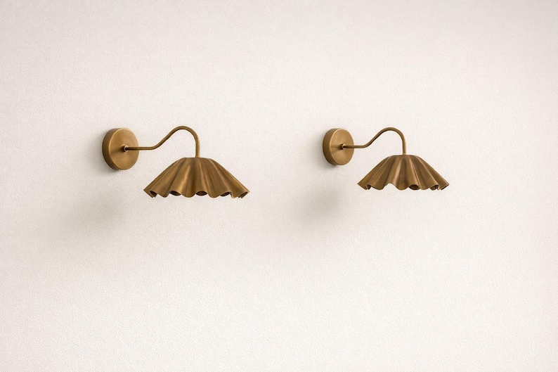 Pair of vintage brass wall sconces with downward, ruffled shades and curved arms, antique brass finish.