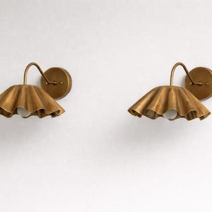 Pair of vintage brass wall sconces with downward, ruffled shades and curved arms, antique brass finish.