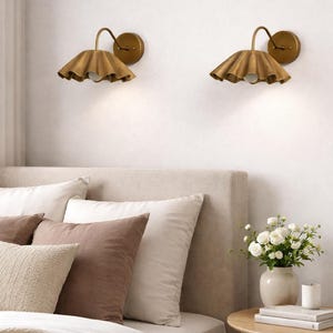 Pair of vintage brass wall sconces with downward, ruffled shades and curved arms, antique brass finish.