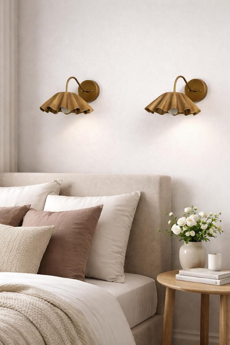Pair of vintage brass wall sconces with downward, ruffled shades and curved arms, antique brass finish.