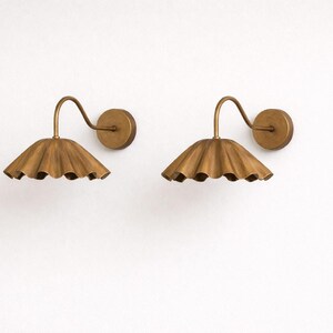 Pair of vintage brass wall sconces with downward, ruffled shades and curved arms, antique brass finish.
