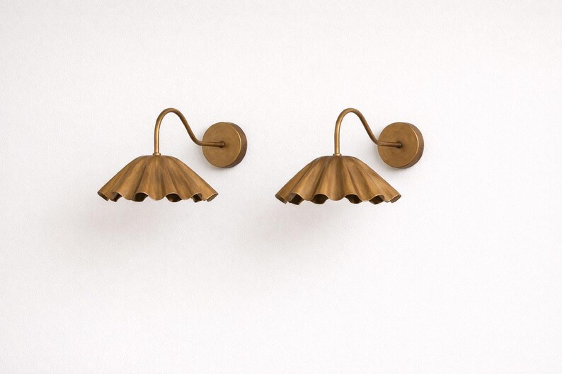 Pair of vintage brass wall sconces with downward, ruffled shades and curved arms, antique brass finish.