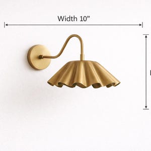 Pair of vintage brass wall sconces with downward, ruffled shades and curved arms, antique brass finish.