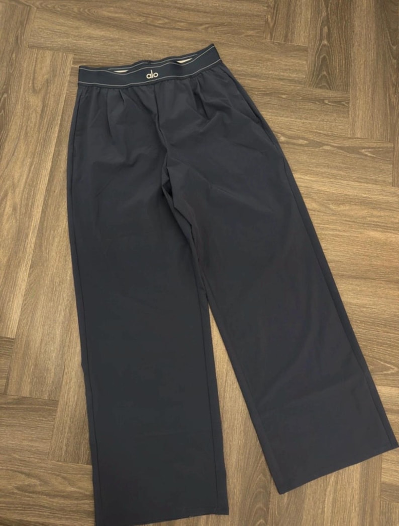 Puede incluir: Pantalones anchos de color azul marino oscuro con cintura blanca y la marca "alo" en blanco. Los pantalones tienen un corte relajado y est&aacute;n hechos de una tela lisa y mate. Los pantalones est&aacute;n doblados cuidadosamente.