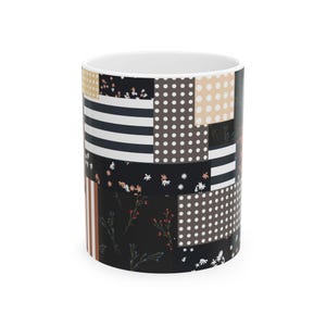 May include: A ceramic mug featuring a patchwork design of black, white, and beige panels. The pattern includes horizontal stripes, polka dots, and small floral motifs in white, red, and blue on a black background, creating a varied geometric look.