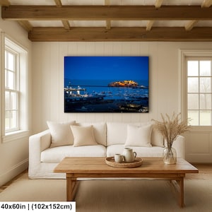 Op de afbeelding: Een grote rechthoekige canvas print met een nachtelijke havenscène. De afbeelding toont een donkerblauwe lucht, een verlicht eiland en boten in het water. De print meet 102x152cm.