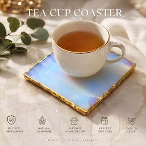 Könnte beinhalten: Ein quadratischer, irisierender Untersetzer mit goldfarbenem, texturiertem Rand, auf dem eine weiße Keramikteetasse mit Goldrand steht. Der Text TEA CUP COASTER ist oben sichtbar, zusammen mit Symbolen für Oberflächenschutz und Reinigung.