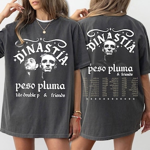 May include: Dark gray t-shirt featuring the text "DINASTIA" above a graphic of two people. Below is "peso pluma" and "tito double p & friends". The back of the shirt has a similar design with a different image.