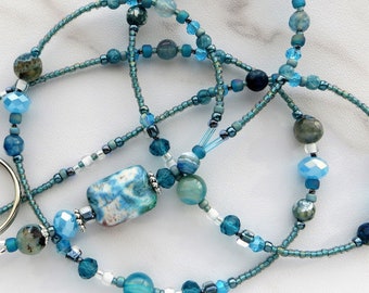 May include: A blue and white beaded lanyard with a blue and white agate pendant. The lanyard is made with various shades of blue beads, including turquoise, teal, and sapphire.