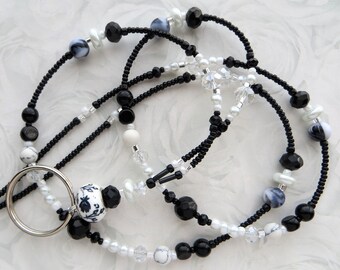 May include: Black and white beaded lanyard with a silver ring and a white ceramic charm with a black floral design.