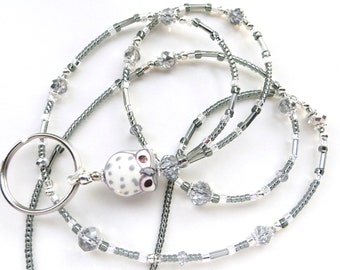 May include: A beaded lanyard with a silver key ring and an owl pendant. The lanyard features gray and silver beads, clear crystal accents, and a white owl pendant with gray spots and pink eyes.