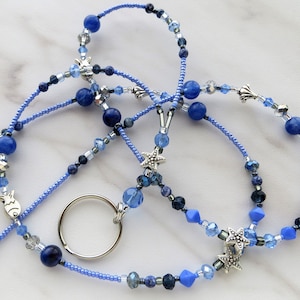 May include: A blue and silver beaded lanyard with a key ring. The beads are various shades of blue and include star and fish charms.