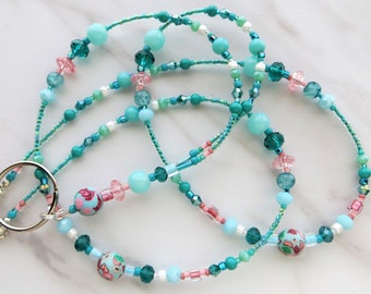 May include: A teal, blue, and pink beaded lanyard with a silver swivel clasp and watermelon patterned beads.