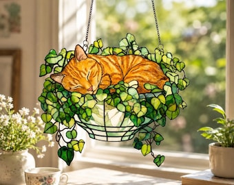 Gato naranja durmiendo en una cesta de monstera, atrapasol acrílico, adorno para ventana estilo vidriera con forma de gato.