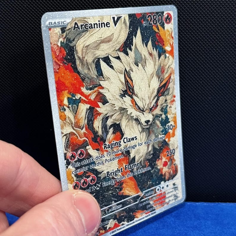 Puede incluir: Una tarjeta coleccionable Pok&eacute;mon Arcanine V hologr&aacute;fica. La tarjeta presenta una ilustraci&oacute;n detallada de Arcanine con acentos blancos, naranjas y rojos. La tarjeta tiene el texto "Arcanine V", "Raging Claws" y "Bright Flame".