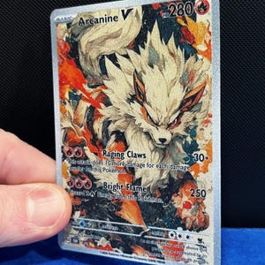 Puede incluir: Carta Pok&eacute;mon Arcanine V hologr&aacute;fica. La carta presenta una ilustraci&oacute;n detallada de Arcanine con pelaje naranja y blanco. El texto de la carta incluye los ataques "Raging Claws" y "Bright Flame", junto con los valores de HP y da&ntilde;o.