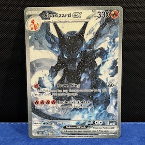 May include: A Charizard EX Pokémon trading card. The card features a black and blue illustration of Charizard with the text "Charizard EX" and "Brave Wing" and "Explosive Vortex". The card has a silver border and the HP is 330.