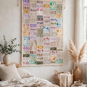 Peut inclure: Une tapisserie murale rectangulaire composée d'un assemblage de carrés de tissu brodés dans des tons de rose, jaune, vert, bleu et blanc, suspendue à une tringle en bois avec des attaches en corde blanche aux coins supérieurs.
