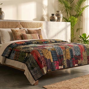 Peut inclure: Un couvre-lit en patchwork composé de divers segments de tissu rectangulaires dans des tons de rouge, bleu, jaune et noir avec des motifs complexes. Le couvre-lit est posé sur un lit avec une tête de lit tressée et des oreillers neutres.