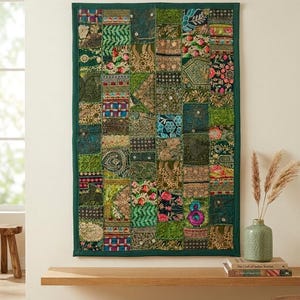 May include: A rectangular wall hanging featuring a patchwork of various green, blue, and gold embroidered fabric squares. The textile displays intricate floral and geometric patterns with metallic thread accents, all enclosed within a solid dark green border.