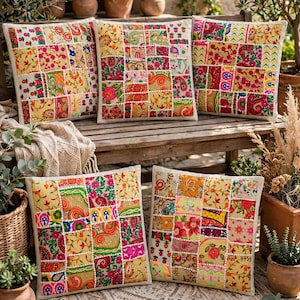 Op de afbeelding: Vijf vierkante sierkussens met een patchworkontwerp van diverse kleurrijke stoffen vierkanten met bloemen-, paisley- en geometrische patronen. Elk vierkant is omlijnd met wit kralenborduurwerk, wat zorgt voor een getextureerd, veelkleurig oppervlak.