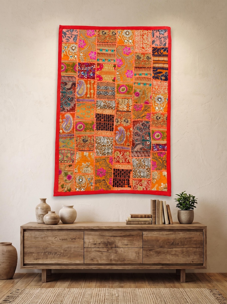 May include: A rectangular wall hanging featuring a vibrant patchwork design composed of numerous small, multi-colored fabric squares. The textile displays intricate embroidery, sequins, and varied floral and paisley patterns in orange, pink, and gold.