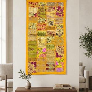 Pode incluir: Uma tapeçaria retangular com um design de patchwork vibrante composto por vários quadrados de tecido amarelos, verdes e cor-de-rosa. O tecido apresenta padrões florais intrincados, bordados metálicos e detalhes em lantejoulas, emoldurados por uma borda amarela.