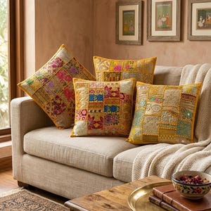 Puede incluir: Tres cojines cuadrados con un diseño de patchwork y bordados intrincados en tonos amarillo, dorado, rosa, azul y verde. Cada cojín tiene un borde amarillo y una superficie texturizada con patrones florales y geométricos.