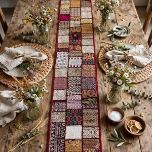 May include: A rectangular table runner featuring a patchwork design of various fabric squares in shades of deep red, gold, white, and purple. Each square displays intricate embroidery, metallic thread detailing, and diverse geometric patterns.