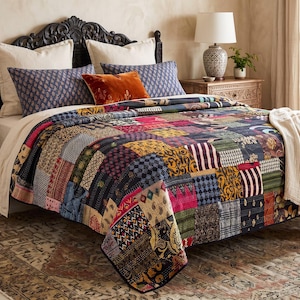 May include: A patchwork quilt featuring a variety of colorful fabric squares with diverse patterns in shades of pink, yellow, blue, and black. The quilt is draped over a bed with a dark carved wooden headboard, cream pillows, and a throw blanket.