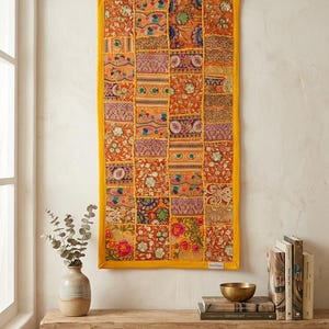 May include: A rectangular wall hanging featuring a patchwork of vibrant orange, gold, and multi-colored fabric squares with intricate floral embroidery, metallic thread accents, and sequins, all framed by a solid yellow fabric border.