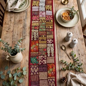 May include: A long, rectangular table runner featuring a patchwork design of various embroidered fabric squares in shades of deep red, gold, green, and cream, with intricate metallic thread detailing and decorative stitching throughout.