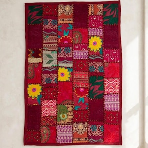 May include: A rectangular wall hanging featuring a patchwork design of various fabric squares in shades of deep red, magenta, and burgundy. The textile includes embroidered floral patterns, yellow flower motifs, and metallic thread accents.
