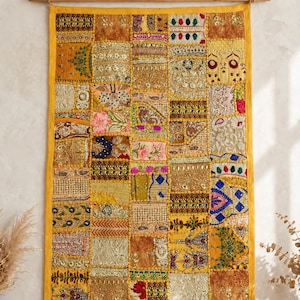Peut inclure: Une tenture murale rectangulaire composée d'un patchwork de carrés de tissu brodés dans des tons or, jaune, rose, bleu et vert. Le textile est suspendu à une tige en bois avec une corde, mettant en valeur un travail complexe de fils métalliques.