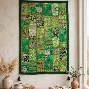 May include: A rectangular wall hanging featuring a patchwork design of various green fabric squares. Each square displays intricate gold and silver metallic embroidery, floral patterns, and paisley motifs. The piece has a dark green border and tassels.