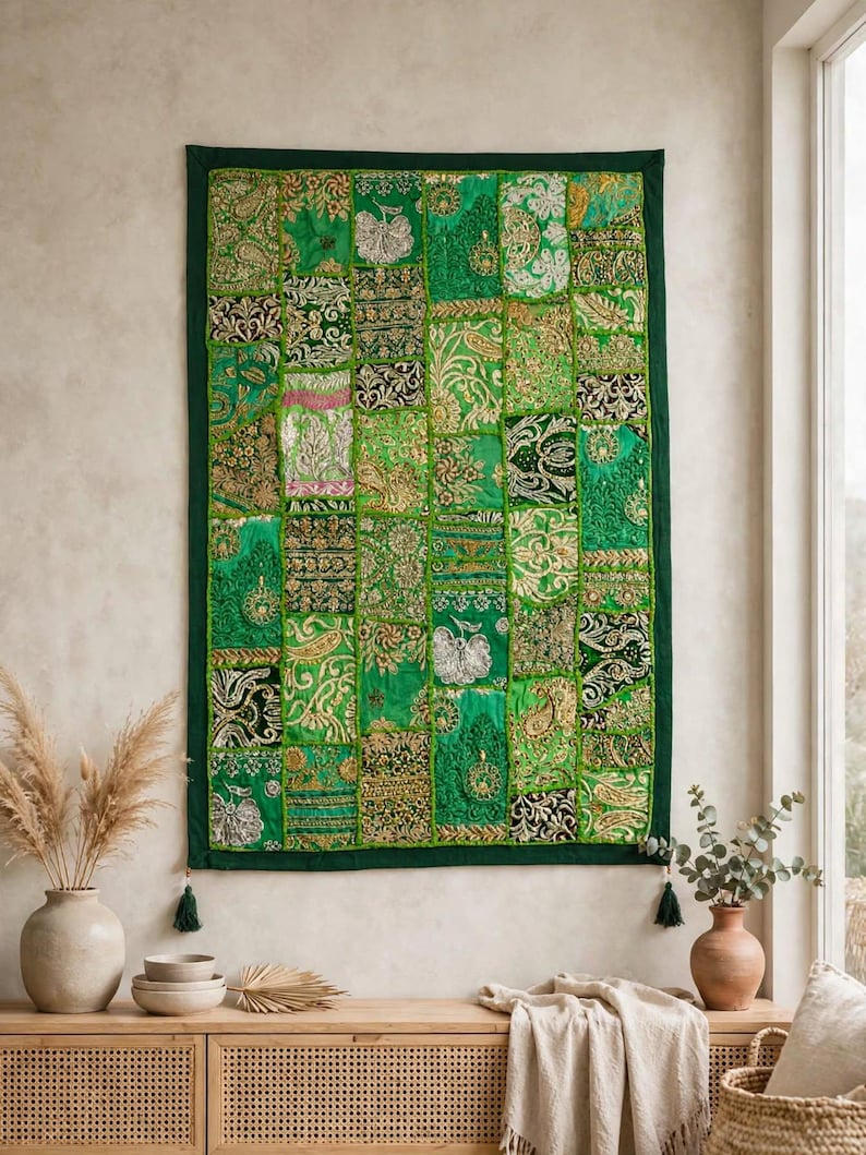 May include: A rectangular wall hanging featuring a patchwork design of various green fabric squares. Each square displays intricate gold and silver metallic embroidery, floral patterns, and paisley motifs. The piece has a dark green border and tassels.