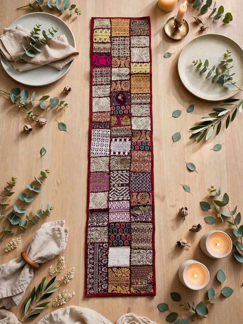 May include: A rectangular table runner featuring a patchwork design composed of numerous small, square fabric panels. The runner displays a variety of intricate textures, metallic gold embroidery, and vibrant colors including deep red, purple, and white.