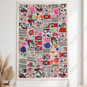 Peut inclure: Une tenture murale rectangulaire composée d'un assemblage de carrés de tissu brodés. Le textile présente une gamme variée de motifs floraux et géométriques aux couleurs vives rouge, bleu, vert, rose et orange, avec des pompons.