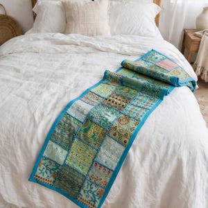 Puede incluir: Un camino de mesa rectangular con un dise&ntilde;o de parches de varios cuadrados de tela en tonos verde y azul cerceta. El camino est&aacute; bordeado con tela azul brillante y decorado con bordados intrincados, hilos met&aacute;licos y peque&ntilde;as lentejuelas.