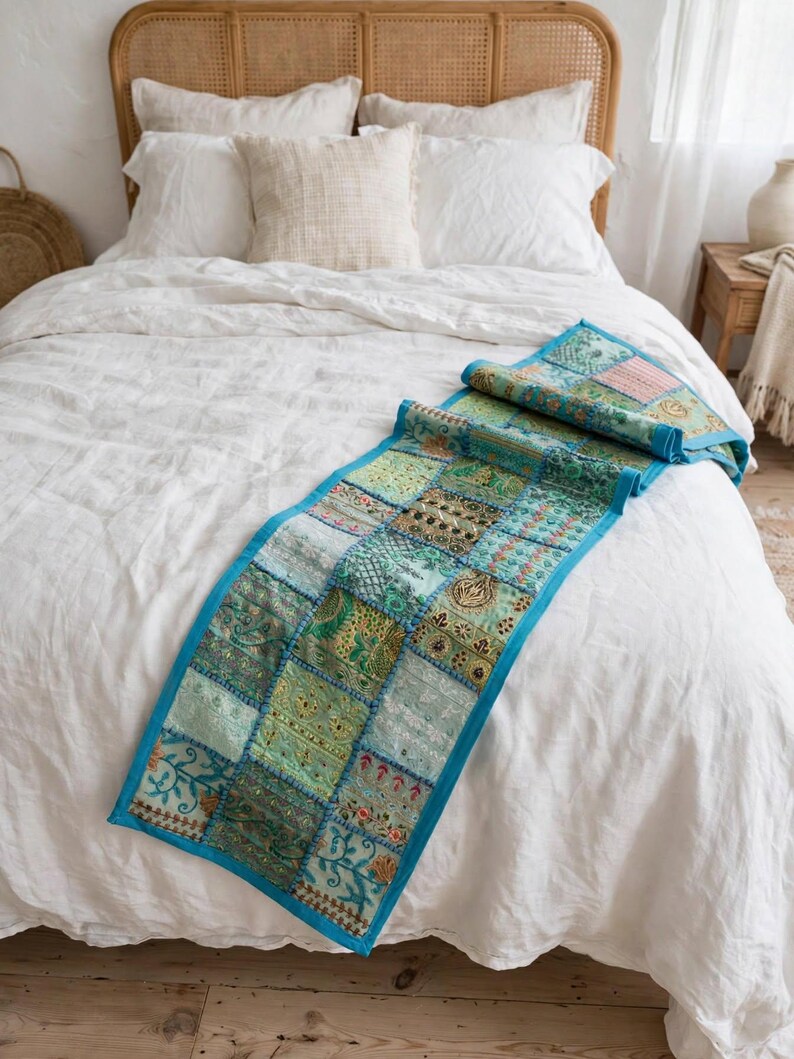 Puede incluir: Un camino de mesa rectangular con un dise&ntilde;o de parches de varios cuadrados de tela en tonos verde y azul cerceta. El camino est&aacute; bordeado con tela azul brillante y decorado con bordados intrincados, hilos met&aacute;licos y peque&ntilde;as lentejuelas.
