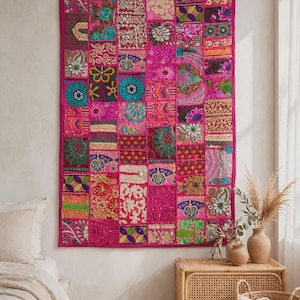 May include: A rectangular wall hanging featuring a patchwork design of various fabric squares in shades of hot pink, magenta, teal, gold, and green. The textile displays intricate embroidery, floral patterns, and geometric shapes throughout.