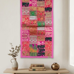 Puede incluir: Un tapiz rectangular con un diseño de patchwork de varios cuadrados de tela en tonos rosa, verde, dorado y rojo. El textil está bordeado por un marco de tela rosa sólida y muestra intrincados bordados y detalles de hilo metálico.