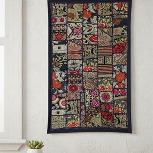 Könnte beinhalten: Ein rechteckiger Wandbehang mit Patchwork-Design. Der Patchwork-Stoff weist verschiedene Blumen- und Paisley-Muster in Rot-, Orange-, Gold- und Grüntönen auf dunklem Blau auf. Die Kanten sind mit einem dunkelblauen Rand eingefasst.