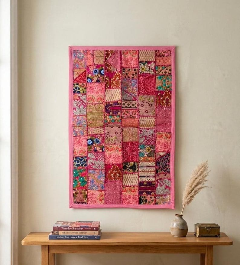 May include: A rectangular wall hanging featuring a patchwork of various pink, magenta, and red fabric squares. The textile displays intricate embroidery, metallic thread accents, and small reflective embellishments, all framed by a solid pink border.