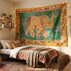 Könnte beinhalten: Ein rechteckiger Wandteppich mit einem großen zentralen Elefantenmotiv, umgeben von einem Patchwork aus grünen, gelben und roten Stoffbahnen mit komplizierten Mustern. Der Wandteppich wird von einer Lichterkette mit kleinen warmweißen Lichtern beleuchtet.