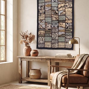 May include: A rectangular wall hanging featuring a patchwork of various fabric patterns in shades of black, white, beige, and muted green. The textile displays intricate geometric and floral motifs arranged in a grid, framed by a solid black border.