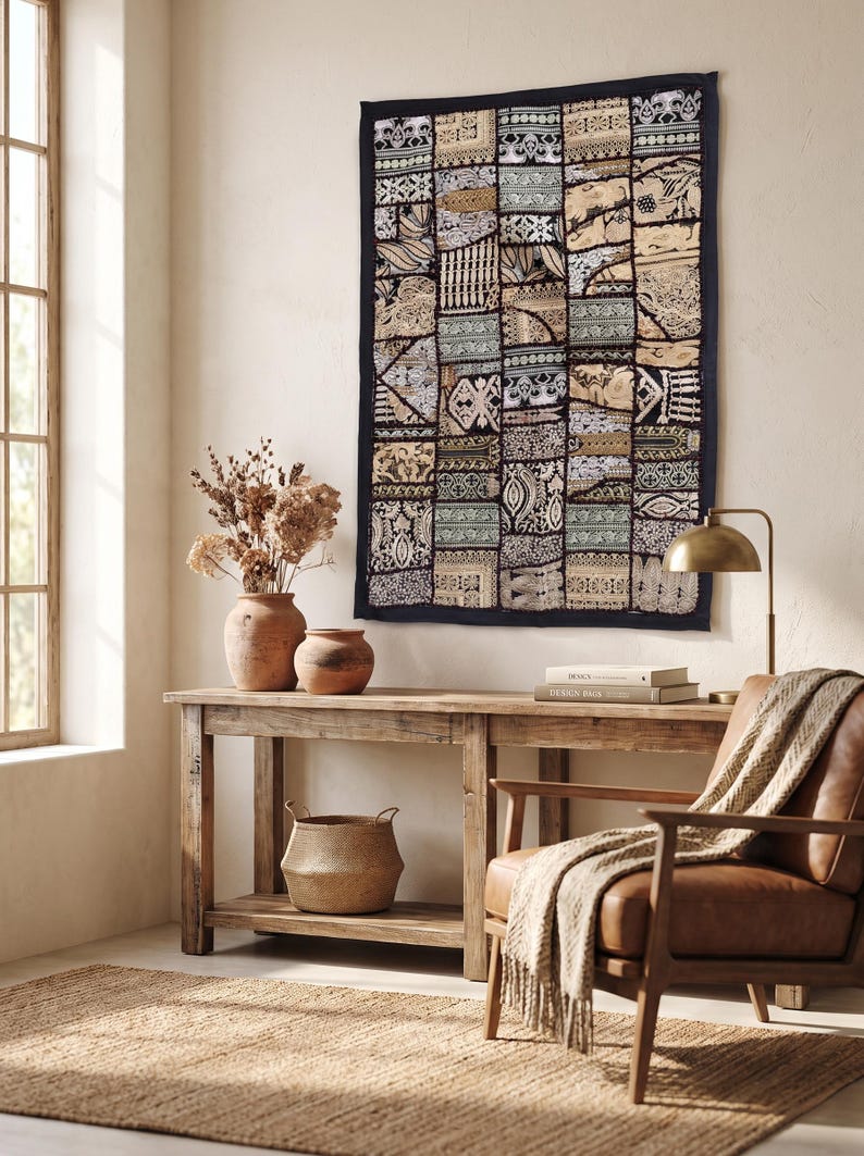 May include: A rectangular wall hanging featuring a patchwork of various fabric patterns in shades of black, white, beige, and muted green. The textile displays intricate geometric and floral motifs arranged in a grid, framed by a solid black border.